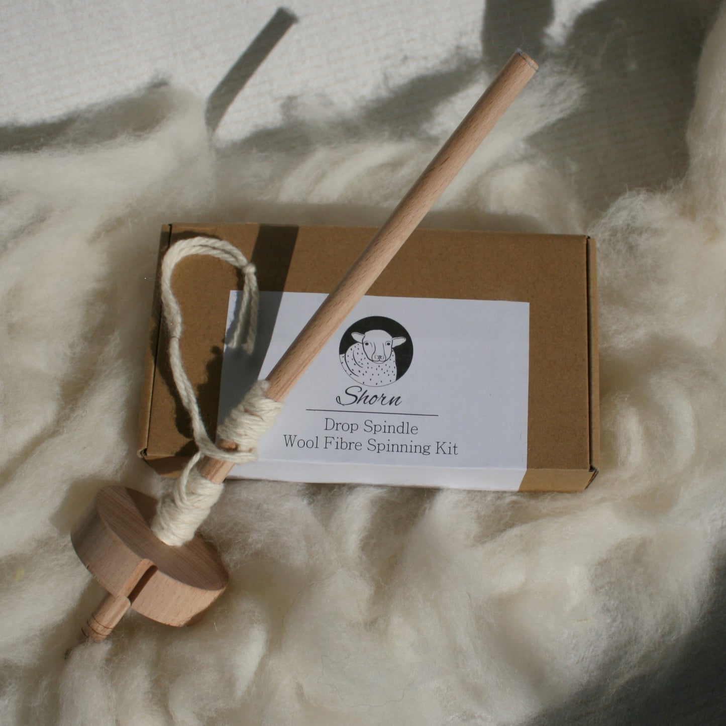Wooden drop spindle top top of cardboard box of other kit pieces