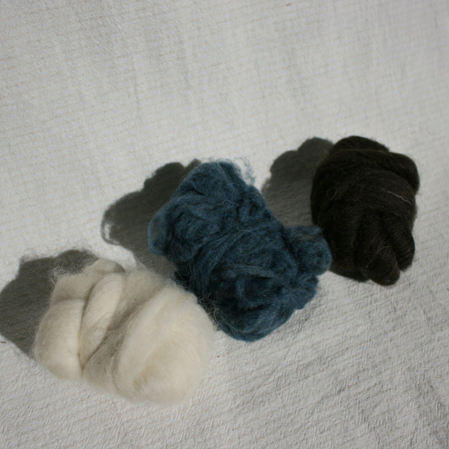Three balls of wool fibres in white, blue, and black on a textured surface